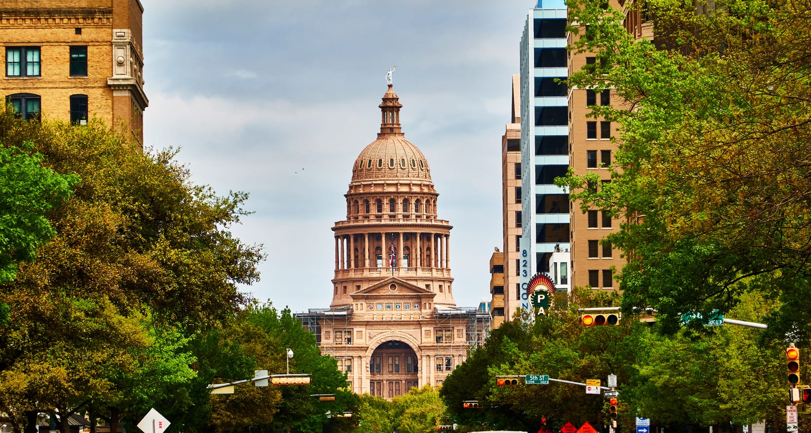 Congress Avenue lined with trees and old buildings, leading to the dome of the Texas State Capitol in Austin
